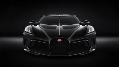 Symmetrical front view of the one-off black Bugatti, the horseshoe grille and red badge centred while the studio behind stays completely dark.