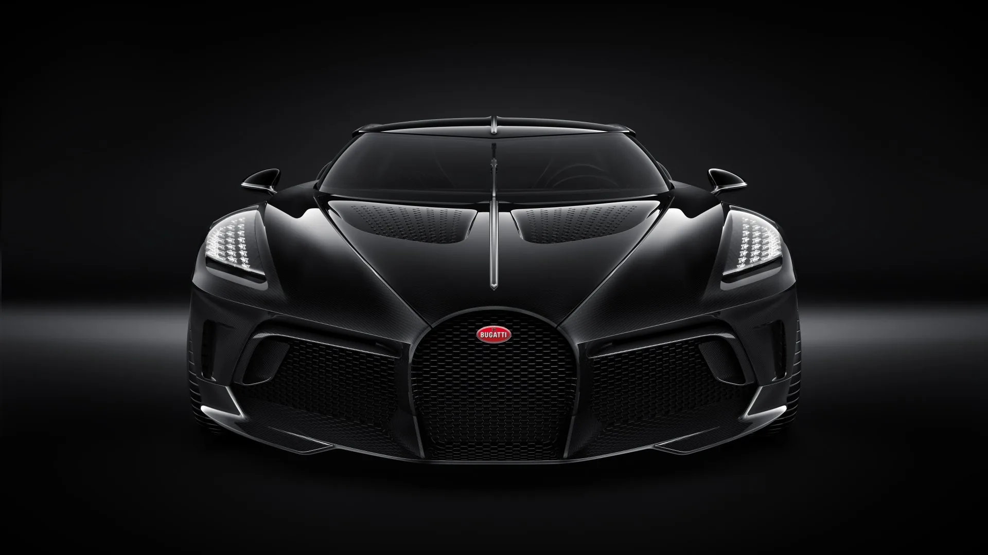 Symmetrical front view of the one-off black Bugatti, the horseshoe grille and red badge centred while the studio behind stays completely dark.