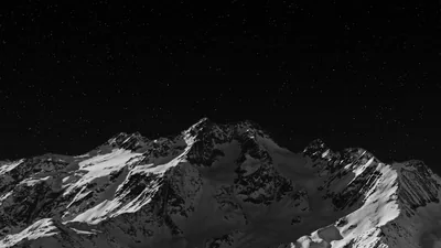 A snow-covered ridge runs across the lower half in monochrome while the sky above stays almost entirely black.