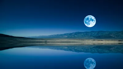 A blue-tinted moon floats over desert mountains mirrored in a shallow salt-flat pool, the clean gradient sky leaving the whole top open.