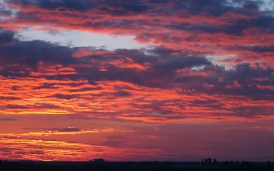 Broken red and orange clouds catch the last light above a flat black horizon, a few small building silhouettes visible at the bottom edge.