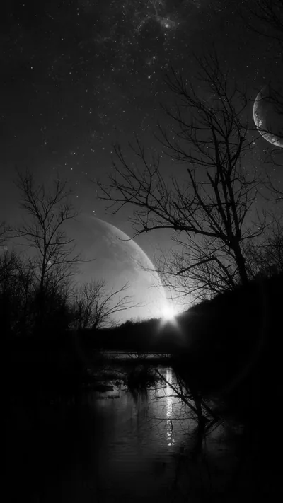 Two moons hang in a starry monochrome sky above leafless branches, their light streaking down a still river below.