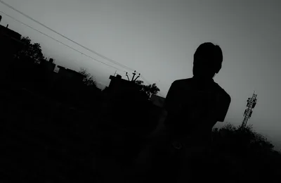 Heavy film grain covers this underexposed dusk shot of a head-and-shoulders silhouette, power lines crossing the pale grey sky in the upper left.