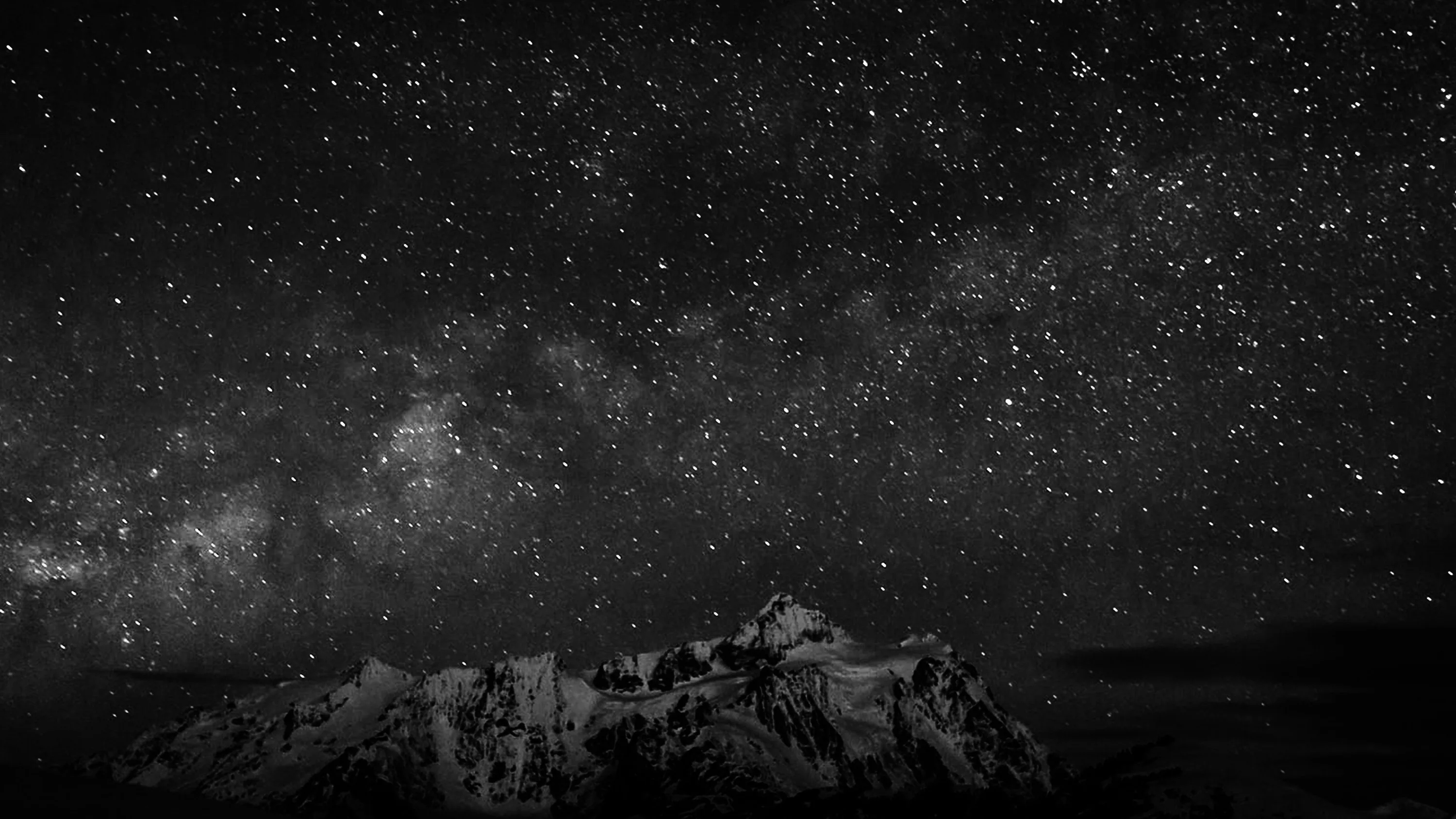 Sharp rock spires break the bottom edge as the galactic band spreads overhead, the whole scene held in grey and black.