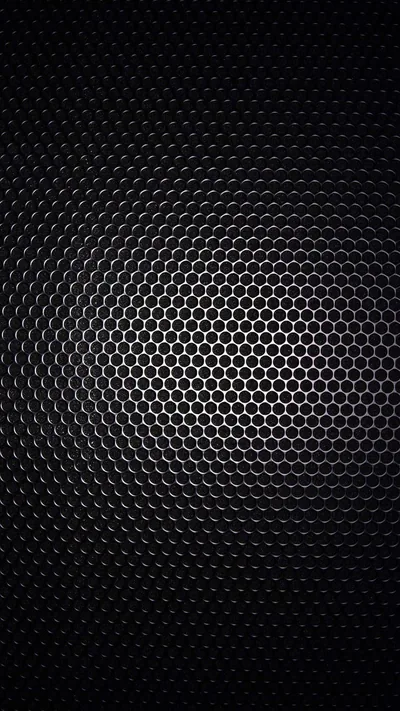 Rows of small hexagonal holes curve across dark metal, brighter at the centre where the light hits and fading out at the edges.