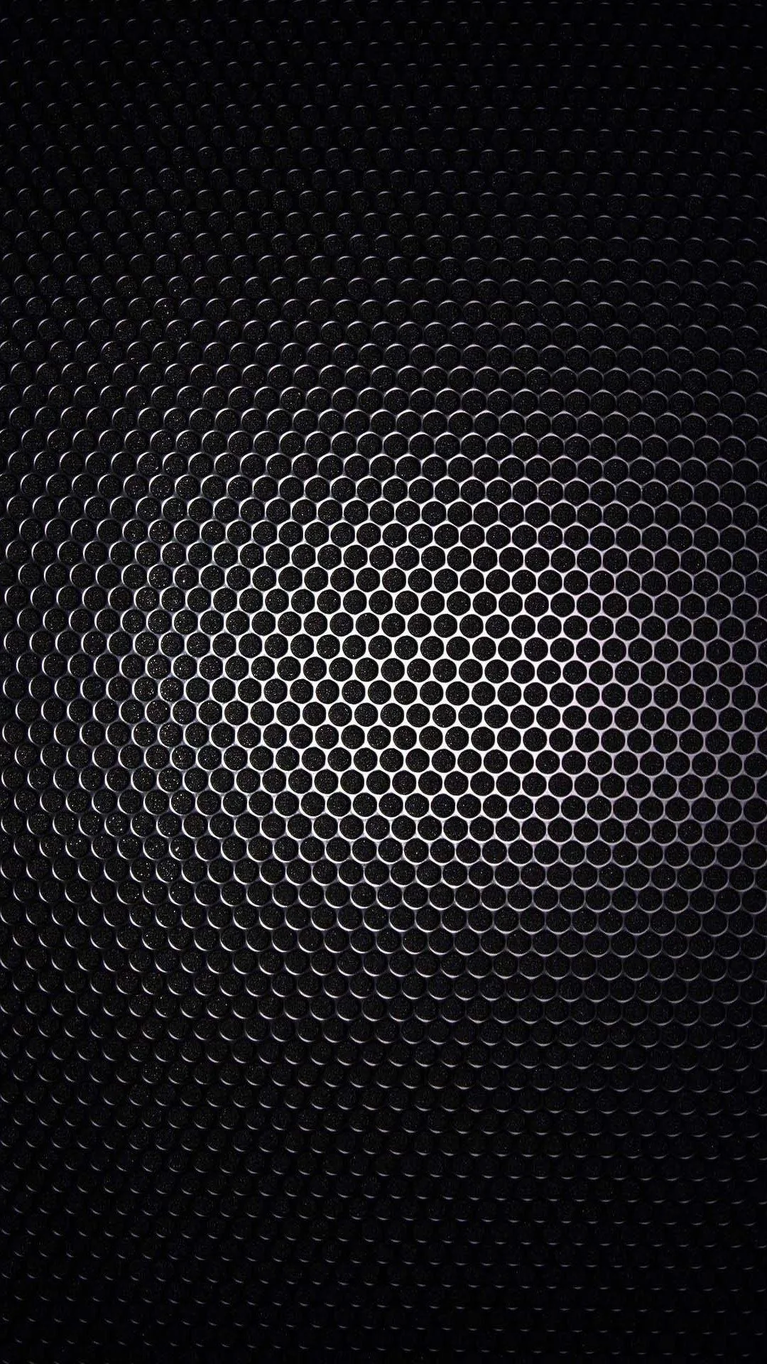 Rows of small hexagonal holes curve across dark metal, brighter at the centre where the light hits and fading out at the edges.