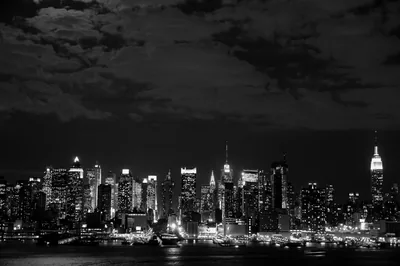 The New York skyline at night in monochrome, lit windows and a heavy cloud bank above the water.
