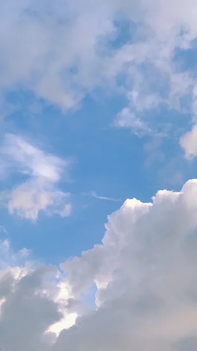 Sunlit cumulus builds along the bottom edge while the upper half stays open blue, leaving plenty of clear space for a phone clock and icons.