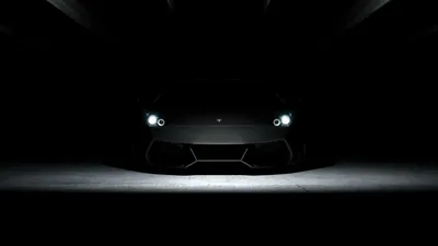 A low sports car sits nose-on in a black space, only its headlights and the light pooling under it visible.
