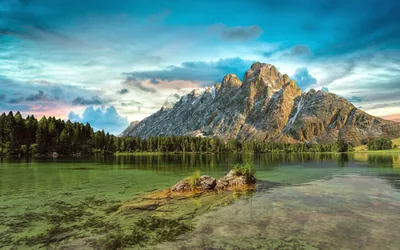 Last light catches a sawtooth summit above weed-streaked shallows, a small rock islet breaking the surface; the muted dusk palette sits easily behind desktop icons.