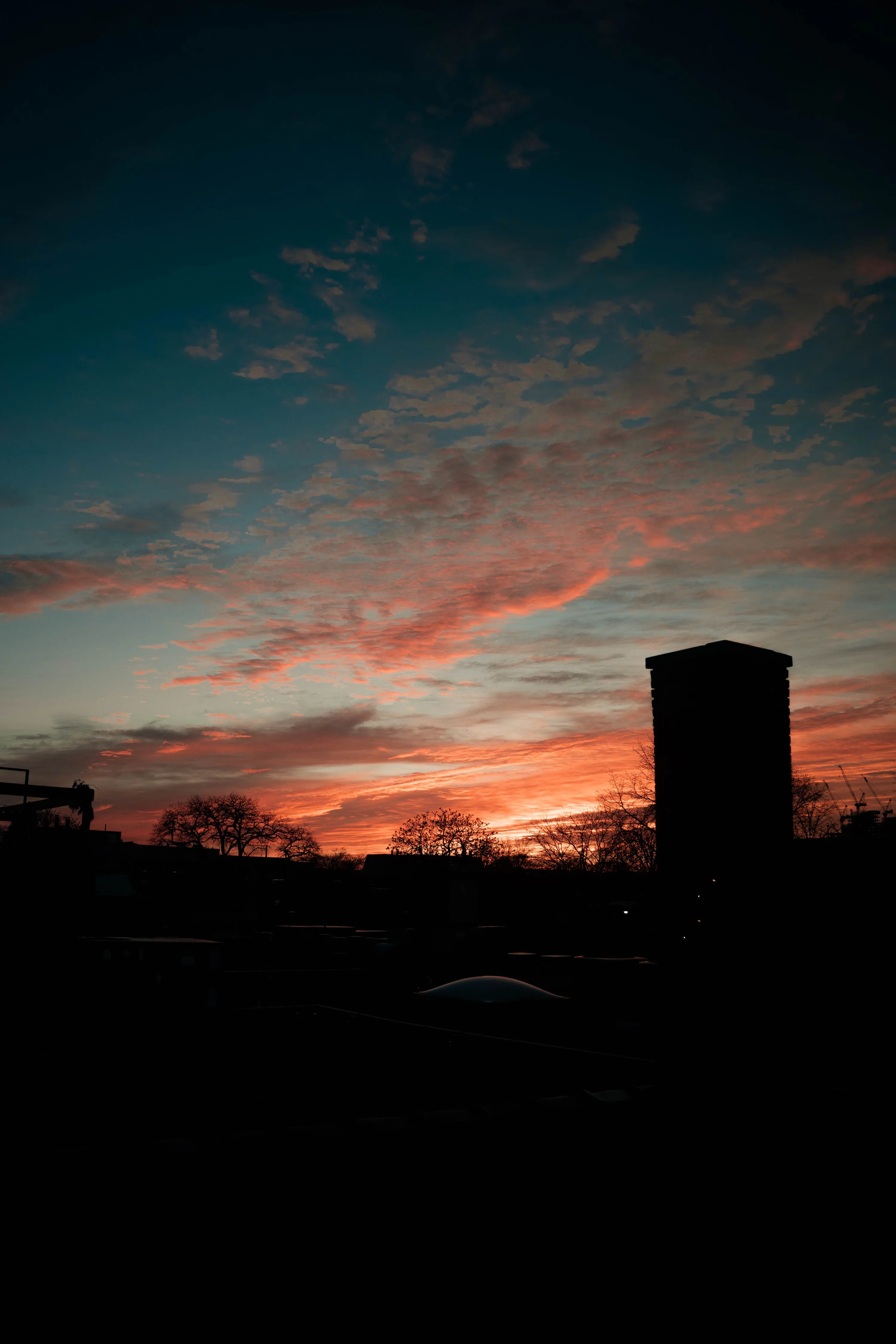 The last red streaks of sunset fade above black silhouettes of a tower and trees, the bottom third solid black for widgets or OLED screens.