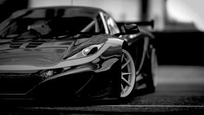 Close crop on the nose of a black McLaren, its headlight and sculpted front wing sharp while the rest of the car and pit wall drift out of focus.