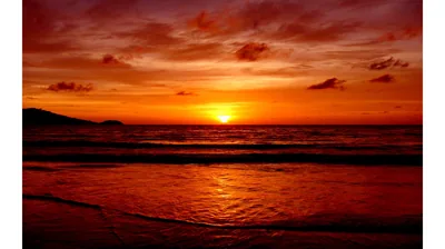 Everything from clouds to wet sand takes on the same deep red as the sun touches the horizon, the shoreline at the bottom fading into shadow.