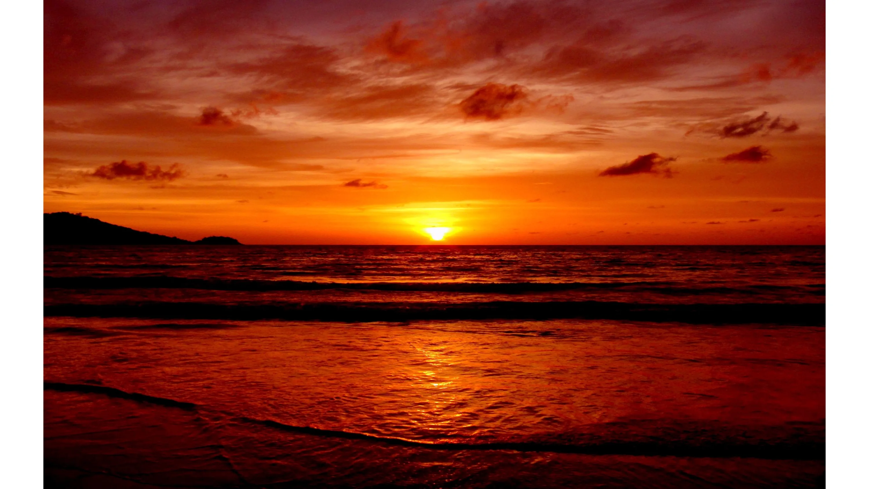 Everything from clouds to wet sand takes on the same deep red as the sun touches the horizon, the shoreline at the bottom fading into shadow.