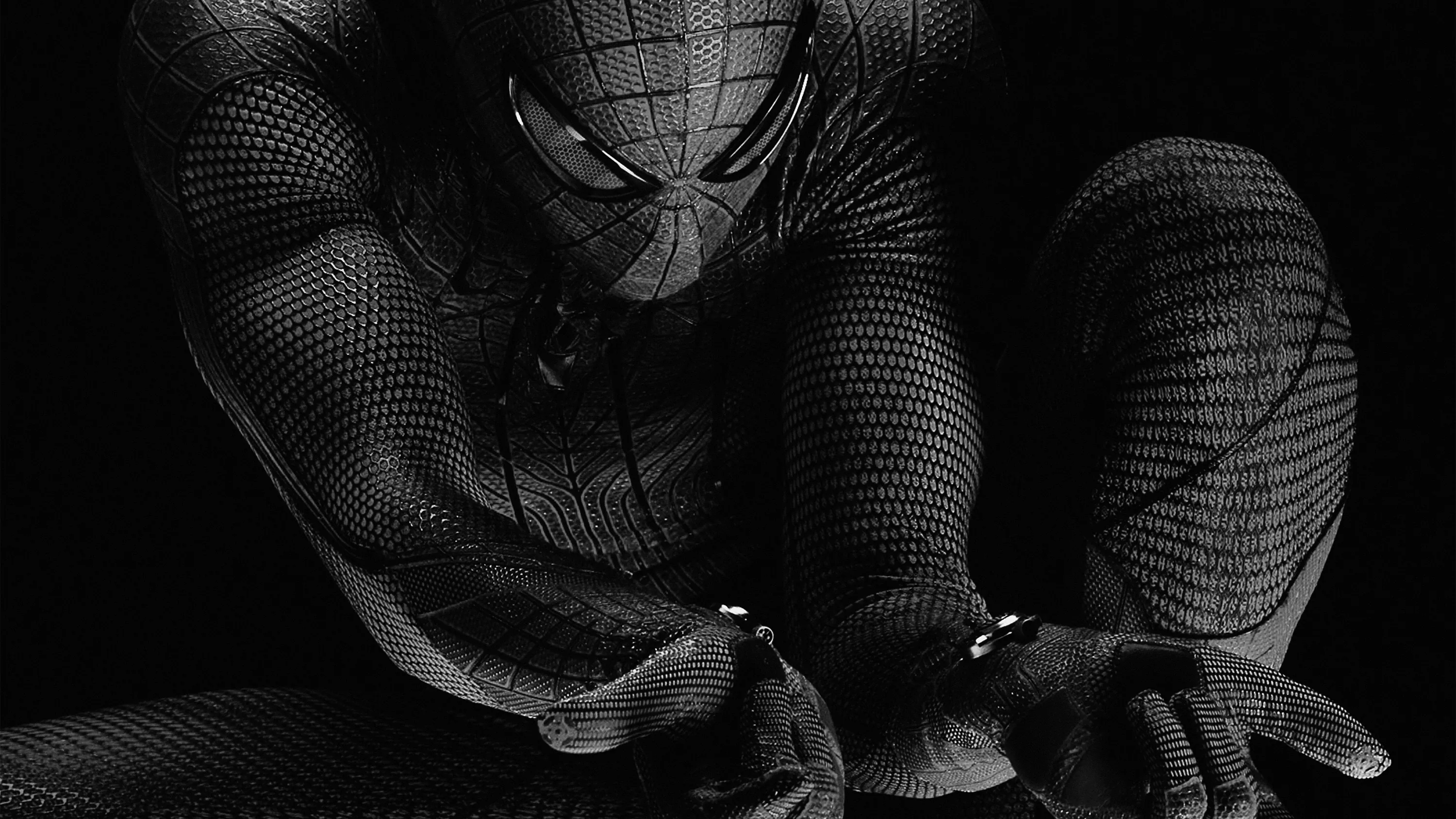 Spider-Man crouches low in a black and white shot, the mesh of the suit sharp and the background dropped to black.