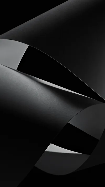 Two sheets of dark paper curl away from each other, the light sliding along one edge and the rest dropping into flat black.