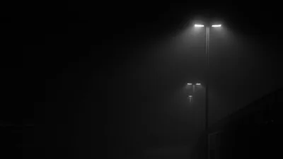 Two paired lamp heads glow through thick night fog in black and white, set in the upper right so the left half stays completely dark.