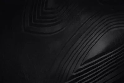 Concentric ridges press through a matte black surface like moulded rubber, lit from the upper left so only the raised edges catch light.