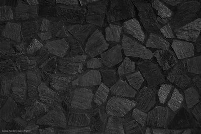 Irregular chunks of charred stone lock together across the wall, each face grained and the gaps between them dropping to black.