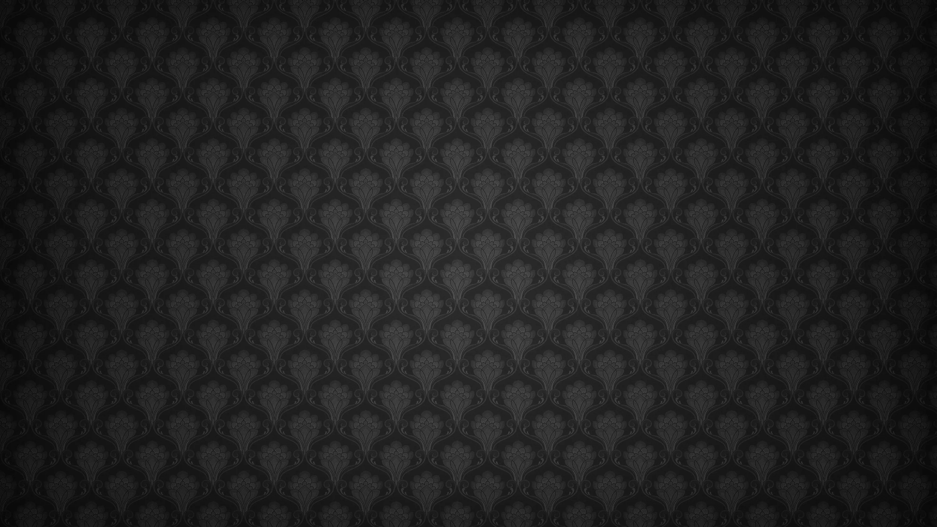 A tiny fan or scallop motif repeats in even rows across charcoal, lit from the centre so the edges of the frame fall away to black.