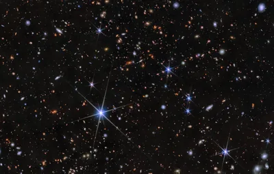 Small orange and white galaxies scattered across deep black, one foreground star throwing six diffraction spikes near the lower left.