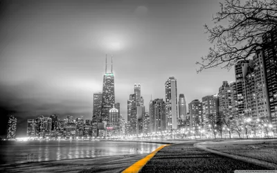 Towers rise in grey haze beyond a curving lakefront road, the painted centre line the one stroke of colour left in the shot.