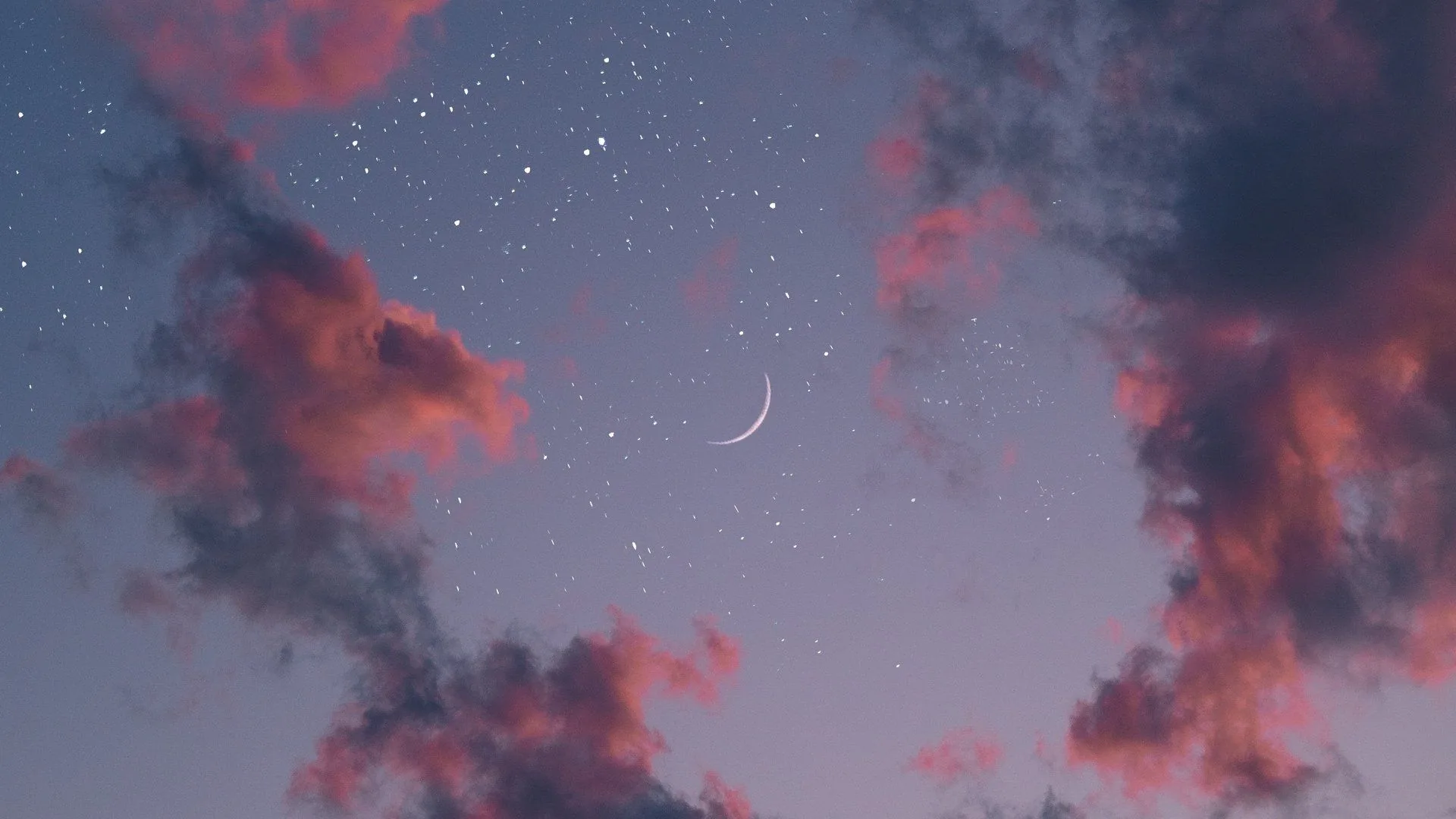 A faint new crescent floats at the centre of a grey-blue dusk, pink-lit cloud wisps pushing in from the corners under early stars.