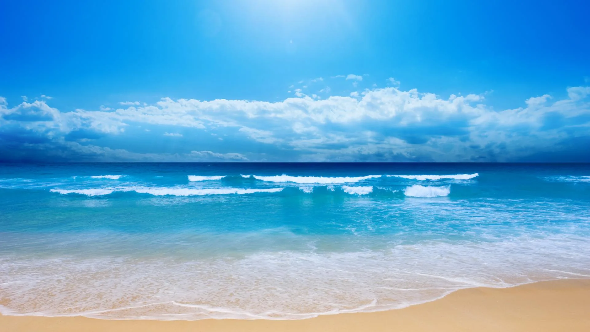 Sun glare floods the top of the frame above small breakers and flat sand, the pale beach strip at the bottom clean enough for desktop icons.