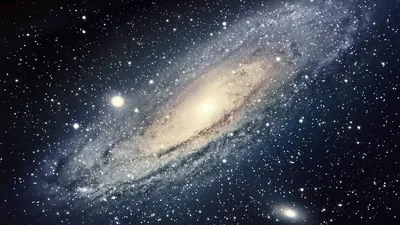 A large spiral fills most of the frame, its golden core fading into blue-white arms and a scatter of foreground stars.
