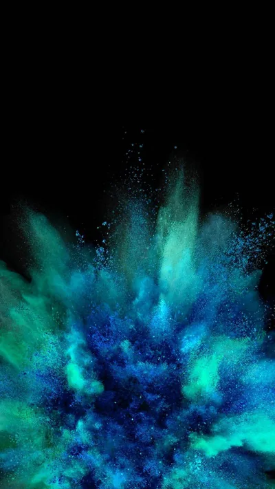 Green and blue pigment bursts upward from the base of the frame, single particles hanging in the black space above the main cloud.