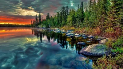 Round stones show through glassy shallows in the lower right while sunset burns orange along the left horizon, the HDR treatment pushing every colour hard.