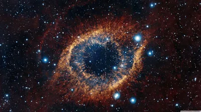 The eye-shaped Helix Nebula glows in rust-orange dust around a deep blue pupil of gas, bright blue stars scattered across the surrounding black.