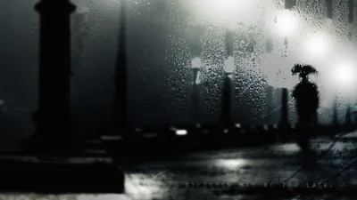 Seen through a rain-soaked pane, lamp flares smear into halos around a dark umbrella shape, the lower band of the frame nearly solid black.