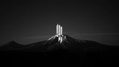 Four tall slabs stand on a snowy summit in monochrome, the surrounding ridges dropping into black.