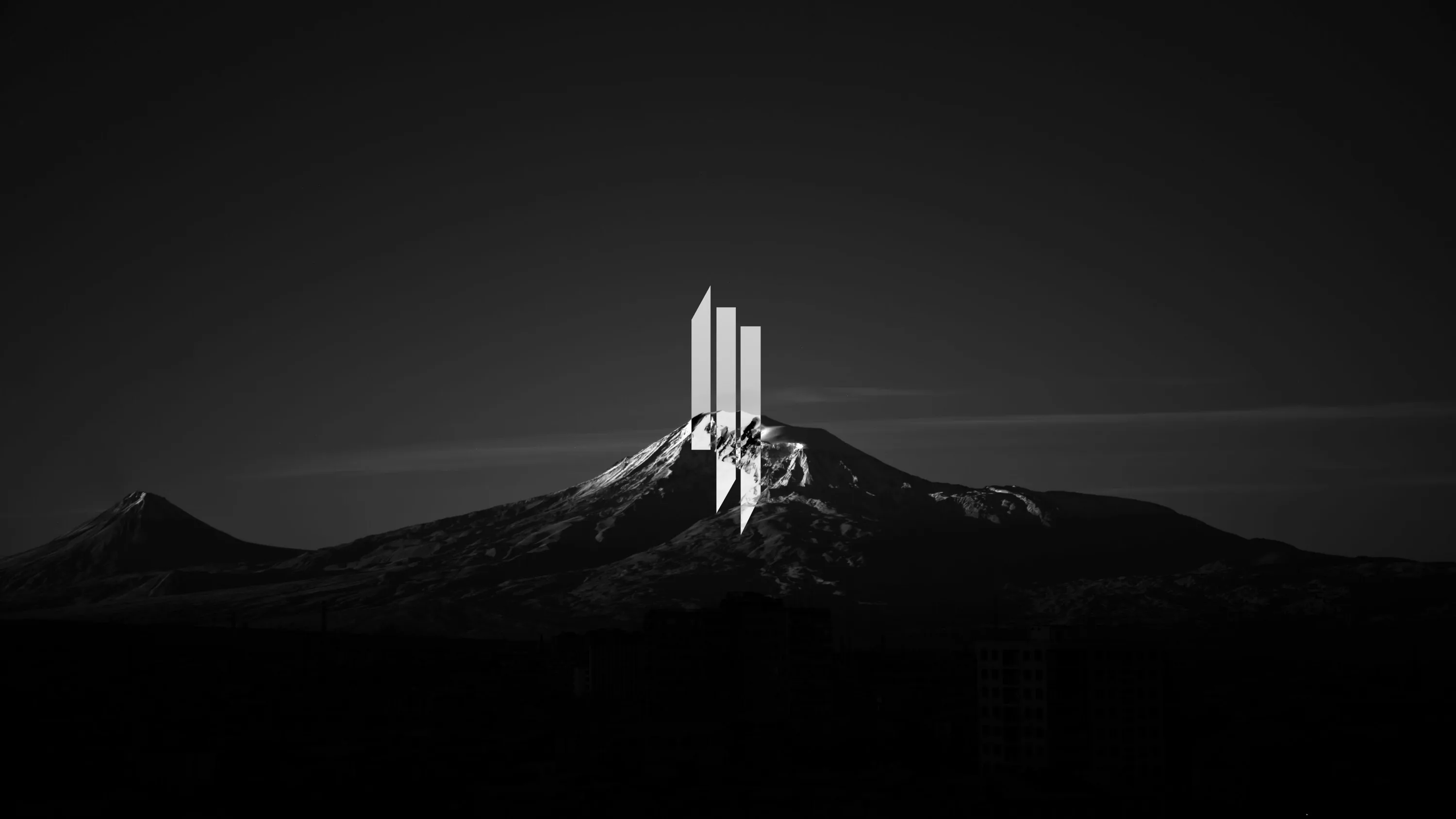 Four tall slabs stand on a snowy summit in monochrome, the surrounding ridges dropping into black.