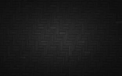 Small rectangular tiles laid in a herringbone weave fill the frame in charcoal, a soft glow behind the centre letting the seams show.