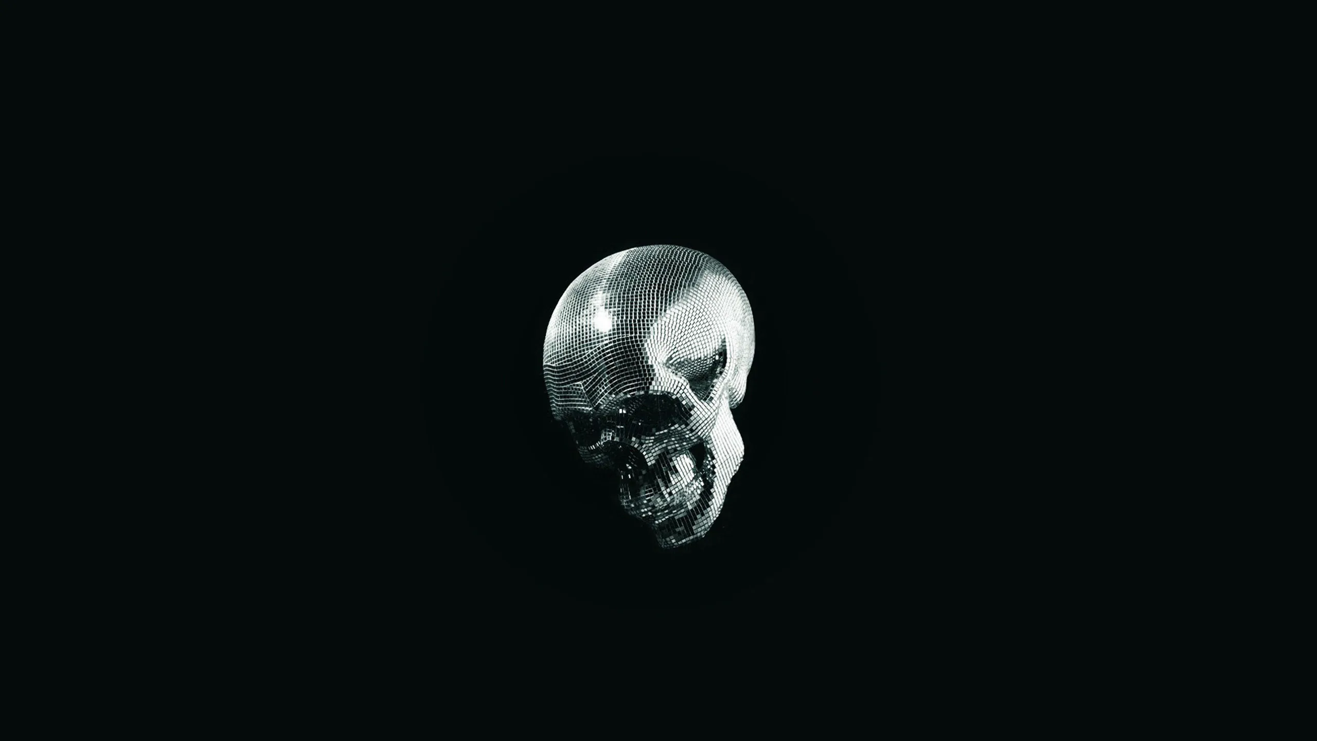 A small metallic skull hangs alone near the middle of an almost entirely black frame, its dented surface catching a weak grey light.