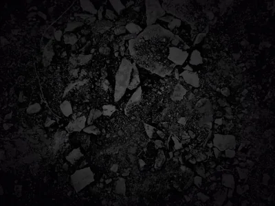 Shattered dark stone fills the frame, lit from above so only the top edges of each fragment show.