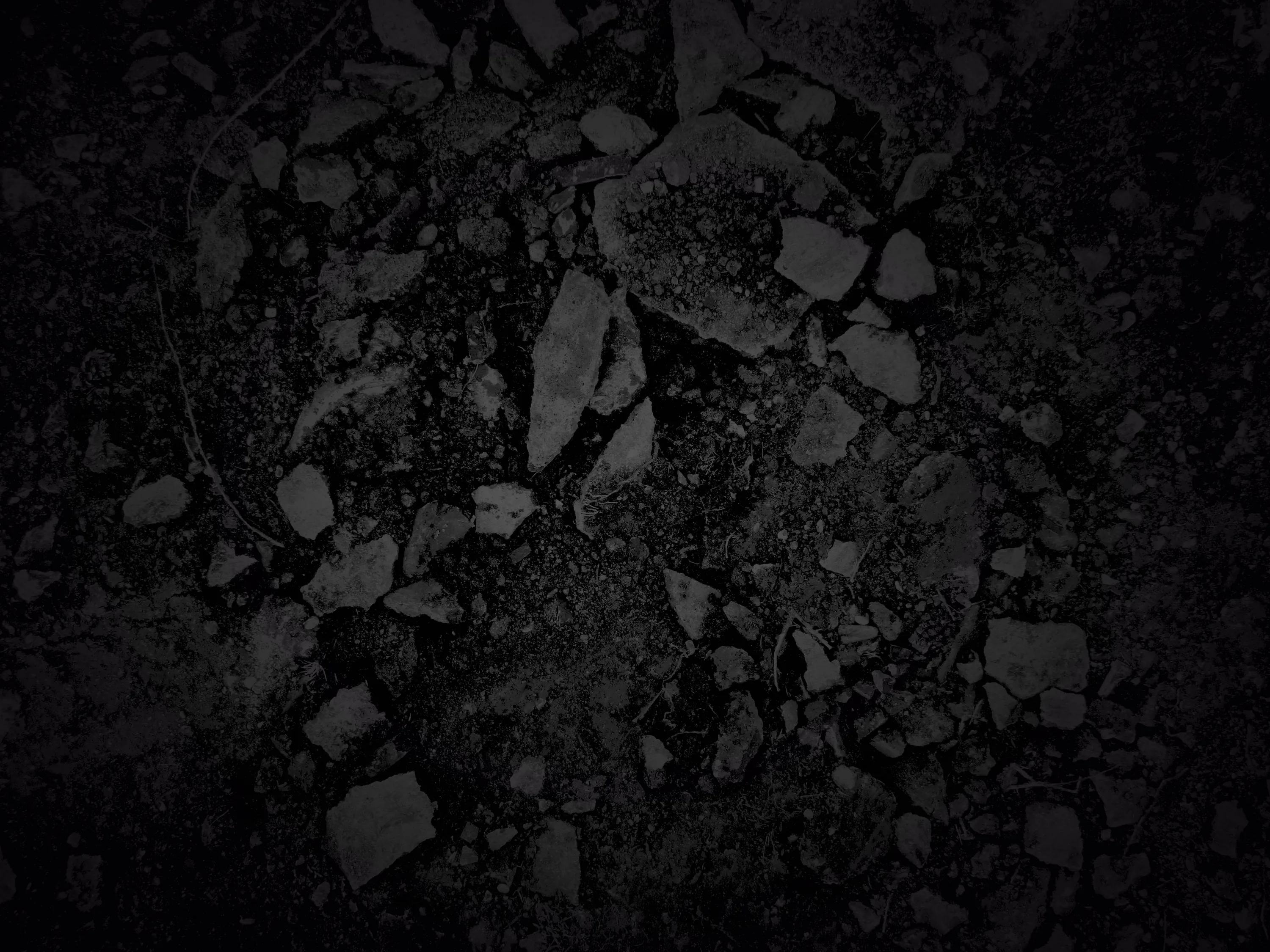 Shattered dark stone fills the frame, lit from above so only the top edges of each fragment show.
