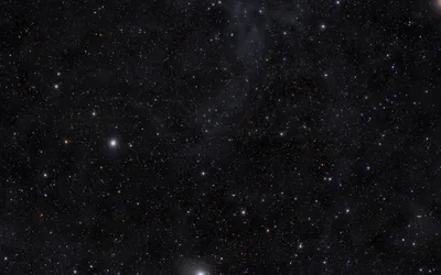 Thousands of small stars scatter across dark space with a faint dust cloud drifting through one corner.