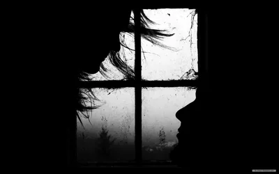 A profile stands black against a fogged windowpane, torn curtain hanging over the cracked glass and the rest of the room lost in shadow.