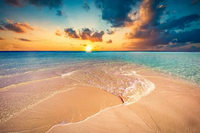 A tongue of pale sand curves between turquoise shallows as the sun drops behind clouds, the foreground beach left open for icons.