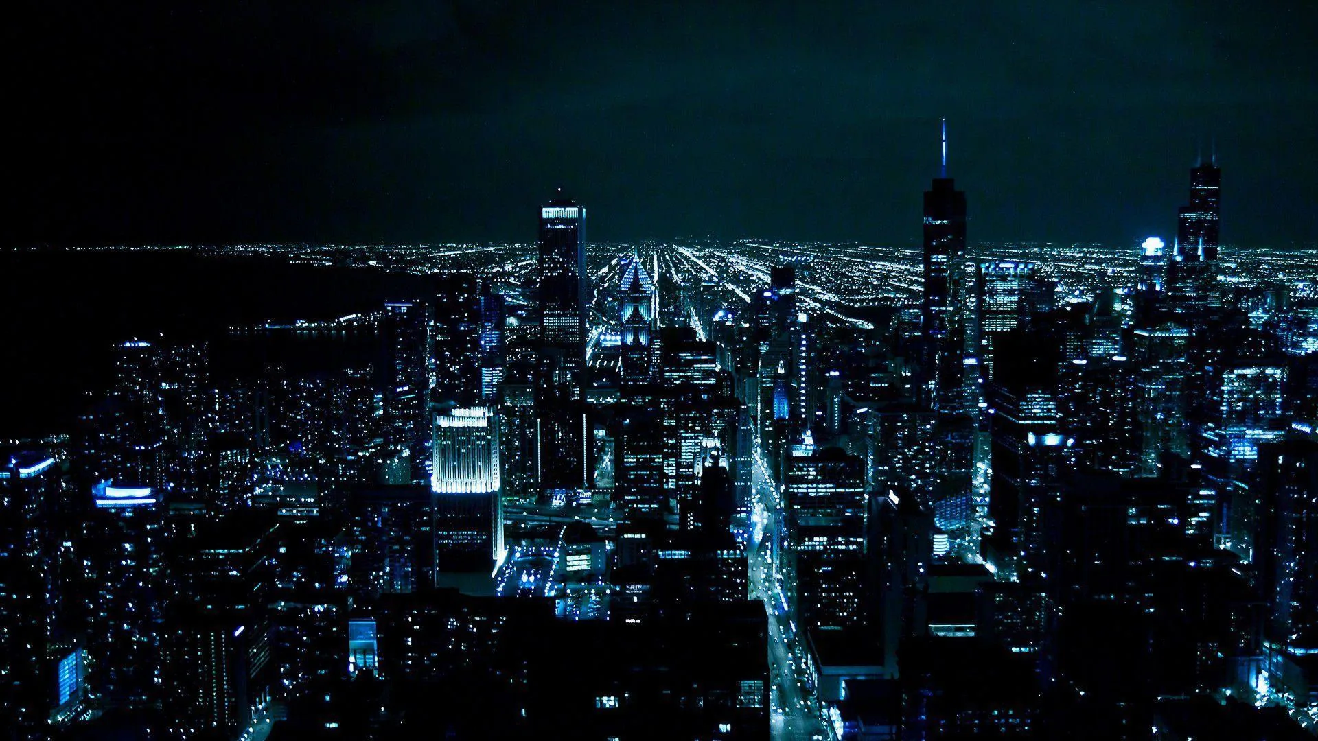 Downtown towers seen from a high vantage, streets running to the horizon as blue-white grids under a black sky.