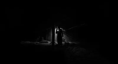 A single silhouette stands in a narrow shaft of light, everything around it lost to black.
