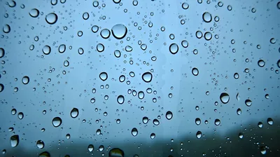 Rain beads hang on a window with a flat grey-blue sky behind, a dark hillside blurring into the bottom right corner of the frame.