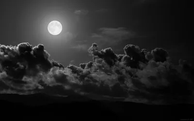 The moon sits high over a bank of cloud in monochrome, hills below reduced to a flat black ridge.