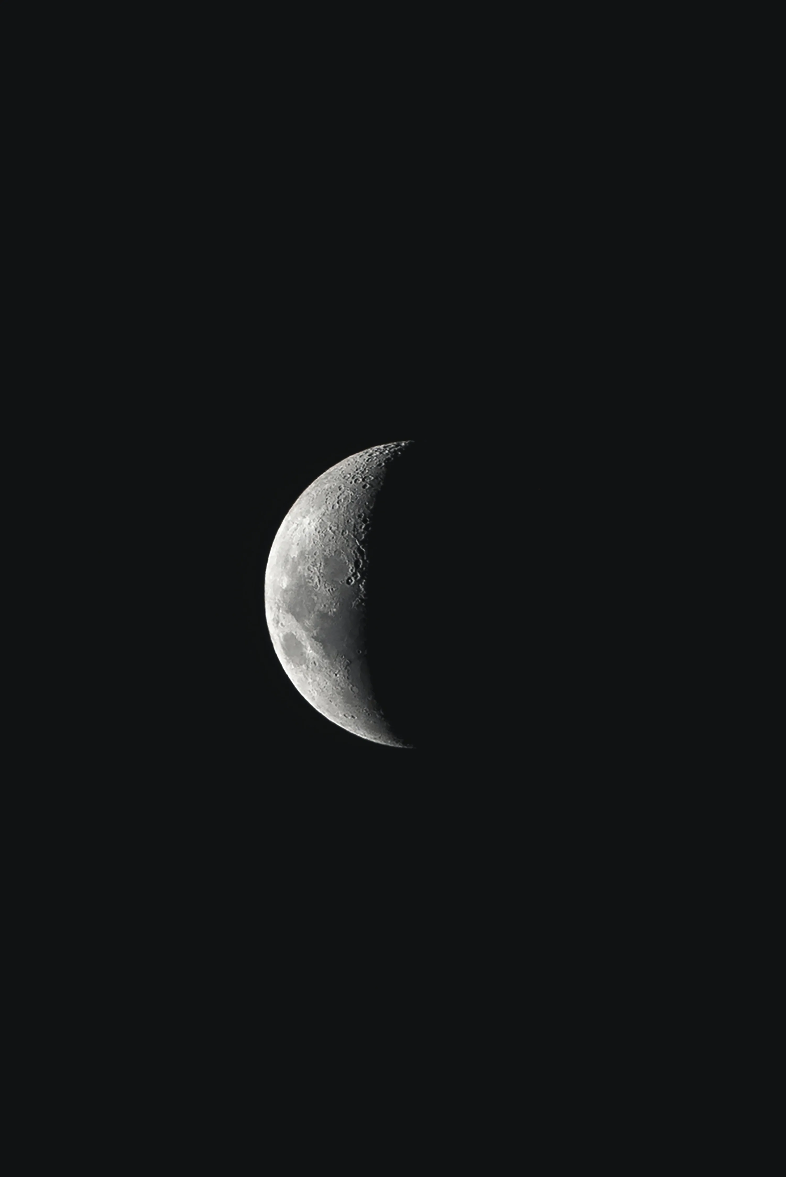 A waning crescent hangs in an otherwise empty black sky, craters visible along the lit edge.