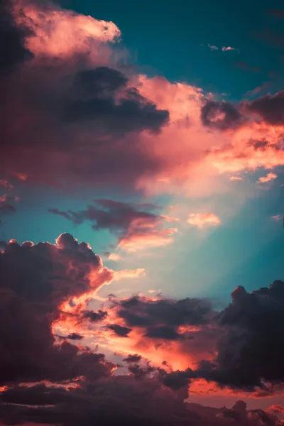 Dark pink-edged storm clouds break apart over a teal sky, a shaft of pale light opening through the centre of the frame.