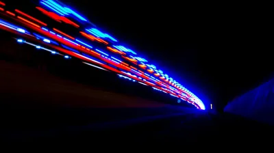 Red and blue light trails streak from the left toward a vanishing point inside a dark tunnel, the right half of the frame dropping to black.