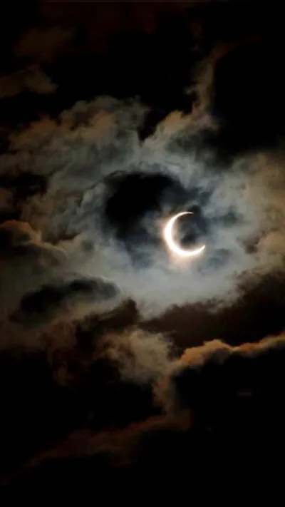 A thin gold crescent burns through a break in heavy night clouds, its light silvering the cloud edges outward while all four corners sink to black.